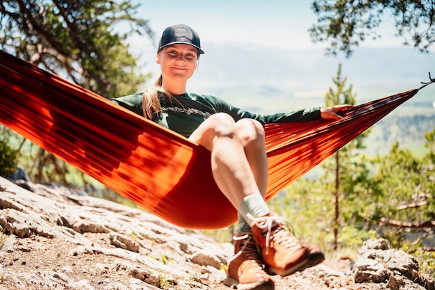 Femme avec capuchon reposant dans un hamac confortable dans les montagnes Se détendre sur un hamac orange entre deux pins en profitant de la vue sur la nature