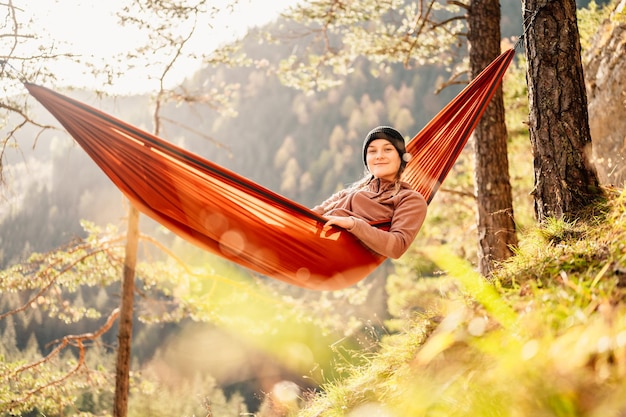 Femme avec capuchon se reposant dans un hamac confortable pendant le coucher du soleil Se détendre sur un hamac orange entre deux pins en profitant de la vue