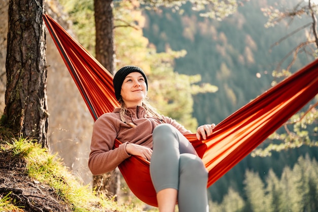 Femme avec capuchon se reposant dans un hamac confortable pendant le coucher du soleil Se détendre sur un hamac orange entre deux pins en profitant de la vue