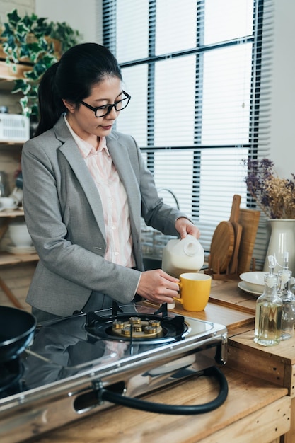 une femme de carrière asiatique a soif et remplit une tasse de lait dans une matinée paisible. une femme chinoise debout dans sa cuisine prend son lait quotidien avant d'aller travailler.