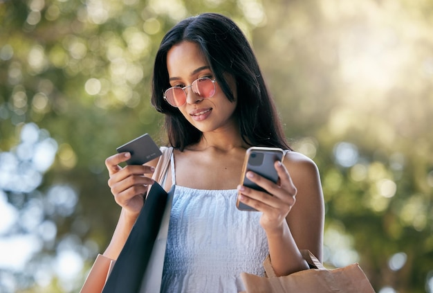 Femme carte de crédit et smartphone pour le commerce électronique sacs de shopping en plein air ou en ligne Jeune cliente latino ou cliente avec téléphone acheter des vêtements ou dépenser pour des produits coûteux ou la vente