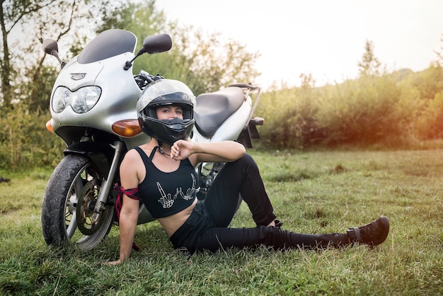 Femme avec casque assis sur l'herbe près de la moto