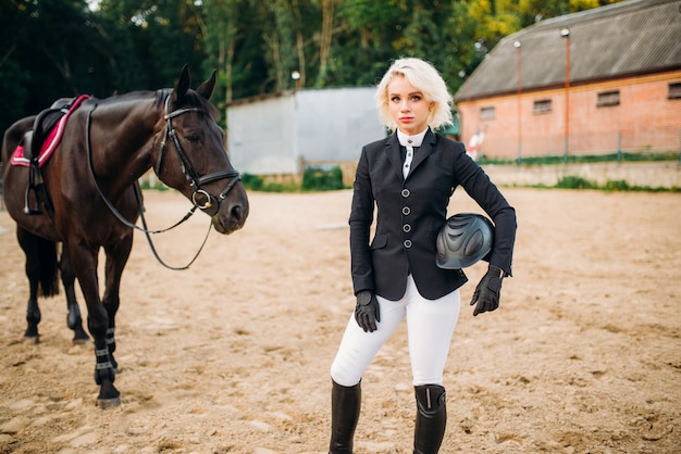 Femme avec casque en mains pose contre cheval