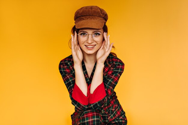 Femme en casquette, lunettes et tenue à carreaux se penche sur la caméra