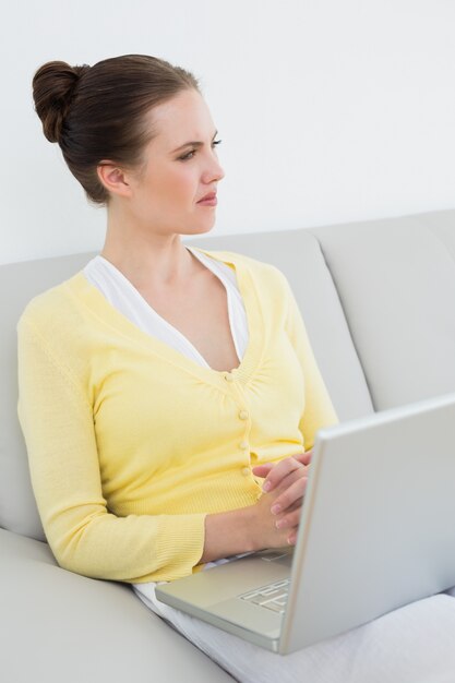 Femme casual réfléchie avec ordinateur portable assis sur le canapé