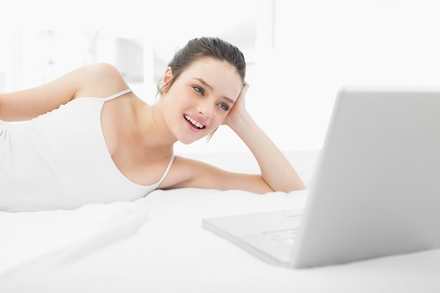 Femme casual souriante regardant ordinateur portable au lit