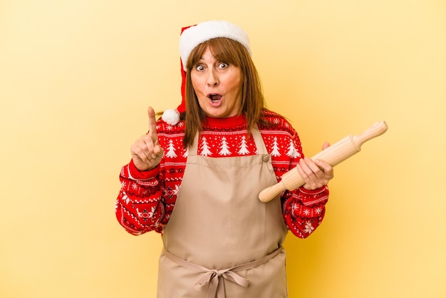 Femme caucasienne d'âge moyen cuisinant des biscuits pour noël isolé sur fond jaune ayant une idée, un concept d'inspiration.