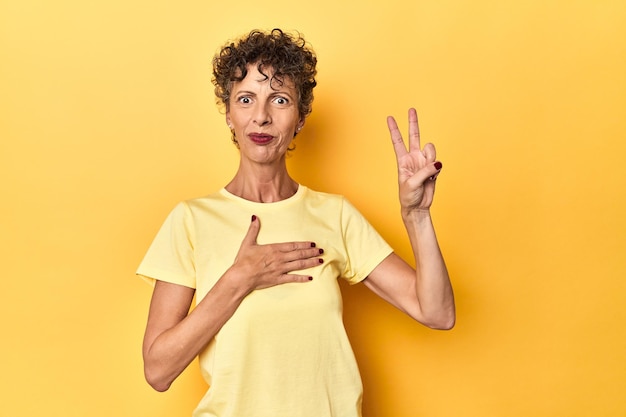 Photo femme caucasienne d'âge moyen sur jaune vif prêtant serment en mettant la main sur la poitrine