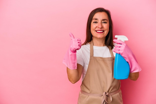 Femme caucasienne d'âge moyen nettoyant la maison isolée sur fond rose souriant et levant le pouce vers le haut