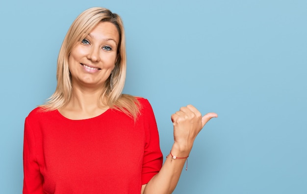 Femme caucasienne d'âge moyen portant des vêtements décontractés souriant avec un visage heureux regardant et pointant vers le côté avec le pouce vers le haut