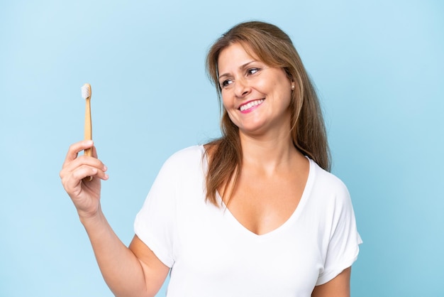 Femme caucasienne d'âge moyen se brosser les dents isolée sur fond bleu avec une expression heureuse