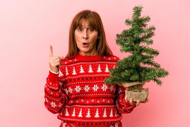 Femme caucasienne d'âge moyen tenant un arbre de Noël isolé sur fond rose ayant une bonne idée, concept de créativité.