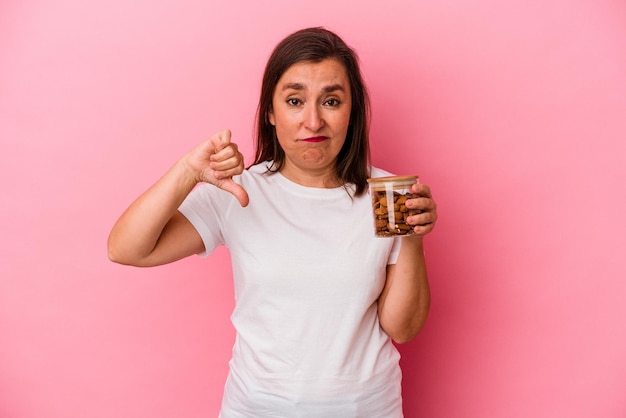 Femme caucasienne d'âge moyen tenant un pot d'amande isolé sur fond rose montrant un geste d'aversion, les pouces vers le bas. Notion de désaccord.