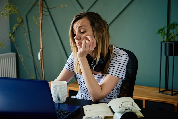 Femme caucasienne assise à table au bureau à domicile et travaille avec un ordinateur portable indépendant travaillant à distance