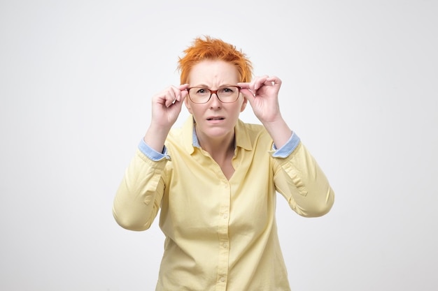 Une femme caucasienne attentive aux cheveux rouges courts regarde scrupuleusement à distance garde la main sur le bord des lunettes