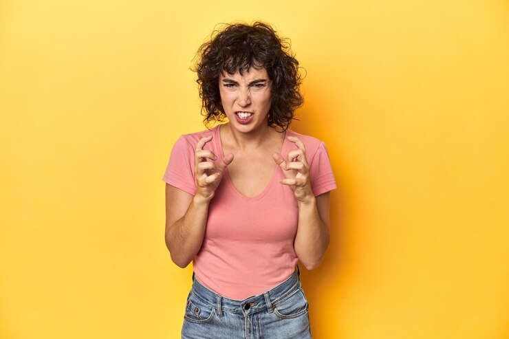 Photo une femme caucasienne aux cheveux bouclés en t-shirt rose hurle avec les mains tendues.