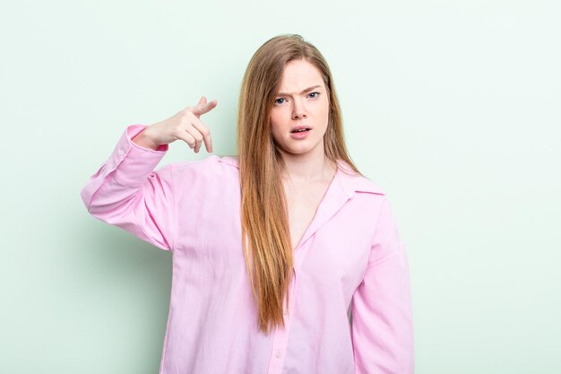 Femme caucasienne aux cheveux roux pointant vers la caméra avec une expression agressive en colère ressemblant à un patron furieux et fou