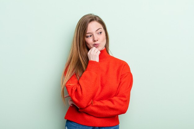 Femme caucasienne aux cheveux roux souriant avec une expression heureuse et confiante avec la main sur le menton, se demandant et regardant sur le côté