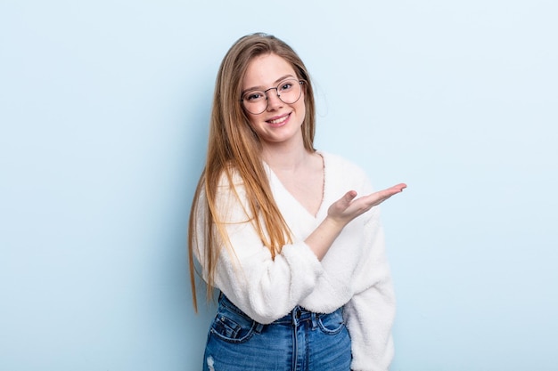 Femme caucasienne aux cheveux roux souriant joyeusement se sentant heureuse et montrant un concept dans l'espace de copie avec la paume de la main