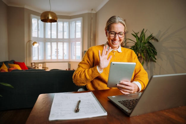 Femme caucasienne ayant un appel vidéo sur tablette numérique et travaillant à domicile