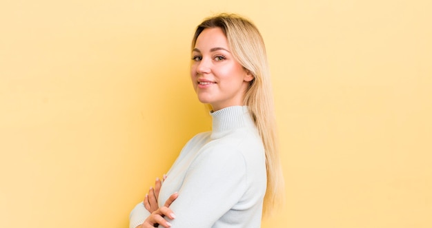 Femme caucasienne blonde souriant à la caméra avec les bras croisés et une vue latérale d'expression heureuse confiante et satisfaite