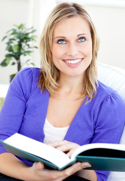 Femme caucasienne brillante, lisant un livre assis sur un canapé