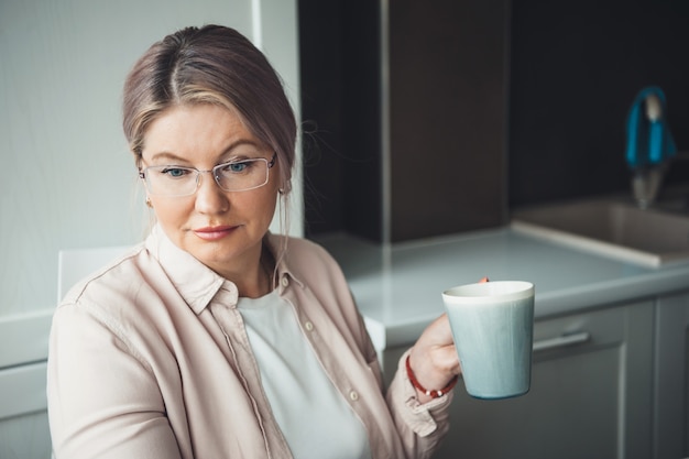 Femme caucasienne concentrée avec des lunettes de boire une tasse de thé et de travailler à distance de la maison