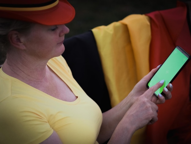 La femme caucasienne dans un chapeau avec le drapeau belge tient un smartphone avec un écran vert