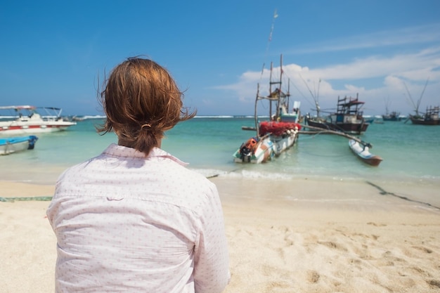 Femme caucasienne debout sur la plage de Midigama et regardant sur l'océan et les bateaux locaux colorés traditionnels