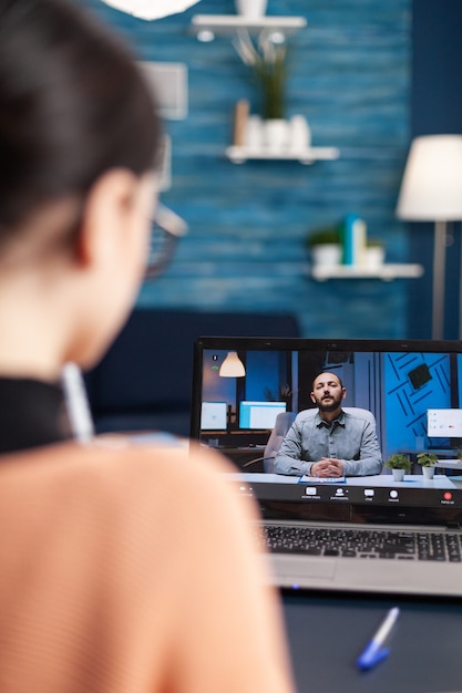 Photo femme caucasienne discutant avec son professeur de mathématiques lors d'une conférence vidéo universitaire à l'aide d'un ordinateur portable. étudiant travaillant à une leçon de communication alors qu'il était assis au bureau dans le salon