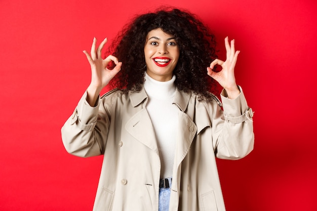 Femme caucasienne élégante en trench-coat montrant un geste correct et souriant satisfait recommandant la compa...