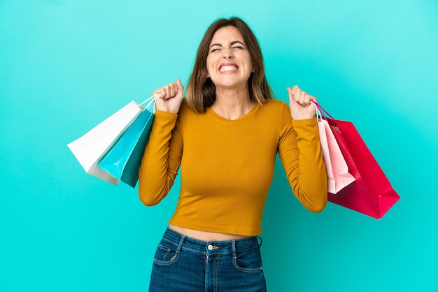 Femme caucasienne isolée sur fond bleu tenant des sacs à provisions et souriant