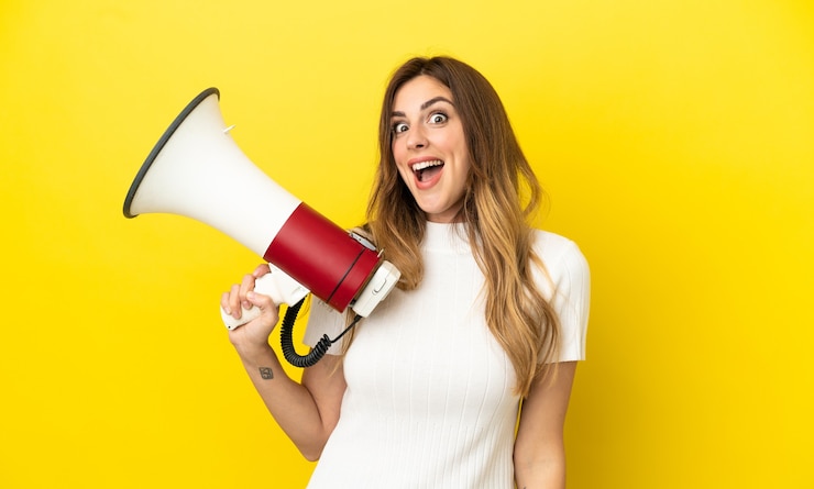 Photo femme caucasienne isolée sur fond jaune tenant un mégaphone et avec une expression de surprise