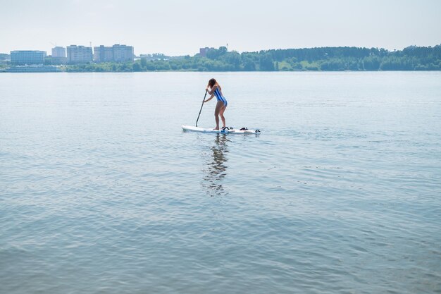 Une femme caucasienne en maillot de bain rayé monte sur un plateau sup la fille préfère le repos actif