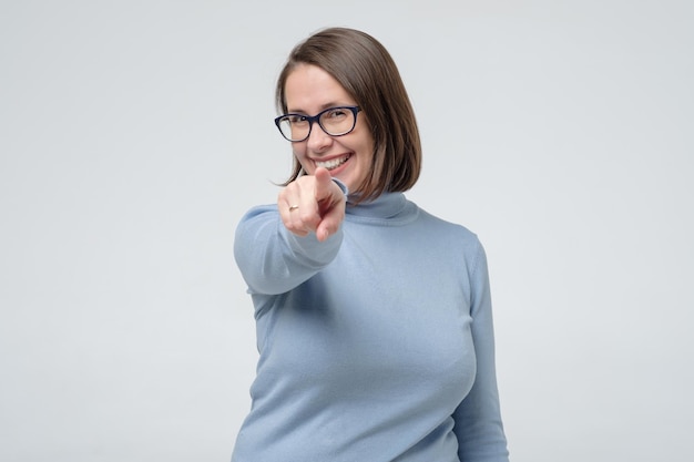 Photo femme caucasienne mature dans des verres et des vêtements bleus pointant sur vous