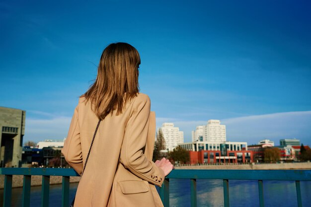 Femme caucasienne millénaire debout au bord de la rivière et profiter d'une journée ensoleillée Touriste féminine portant une tranchée élégante marchant dans la rue de la ville européenne