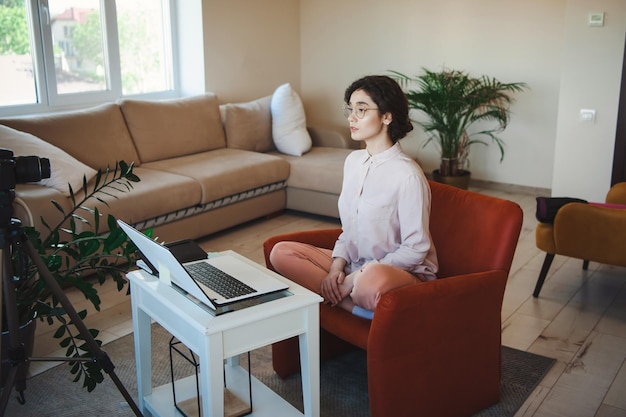 Femme caucasienne avec ordinateur portable participant à la vidéoconférence assise sur un fauteuil à la maison vid...