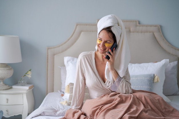 Une femme caucasienne en peignoir est assise dans son lit avec des taches sur son visage faisant