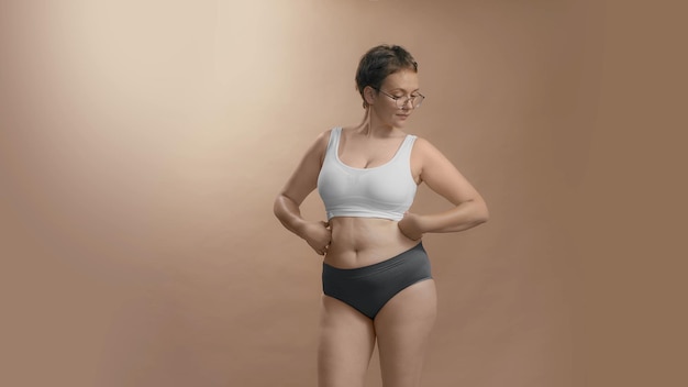 Femme caucasienne positive au corps complet en sous-vêtements apprécier et être fière de ses formes Fond de studio beige photo de haute qualité