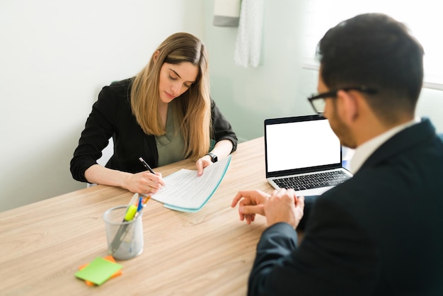 Femme caucasienne professionnelle signant un contrat avec son avocat masculin. Collègue d'affaires féminin écrivant et examinant des documents de travail avec un collègue