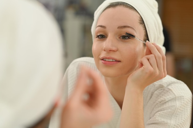 Femme caucasienne souriante appliquant du mascara noir sur les cils Concept de beauté et de cosmétiques