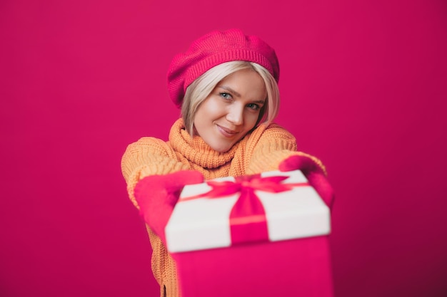 Femme caucasienne souriante en béretstreching une boîte cadeau à la caméra isolée sur fond rose...