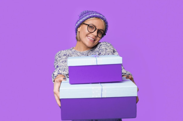 Femme caucasienne souriante donnant deux coffrets cadeaux festifs de Noël isolés sur fond violet souriant...