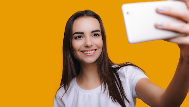 Photo femme caucasienne souriante fait un selfie sur un mur jaune avec un espace vide