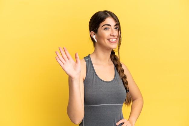 Femme caucasienne sportive isolée sur fond jaune saluant avec la main avec une expression heureuse