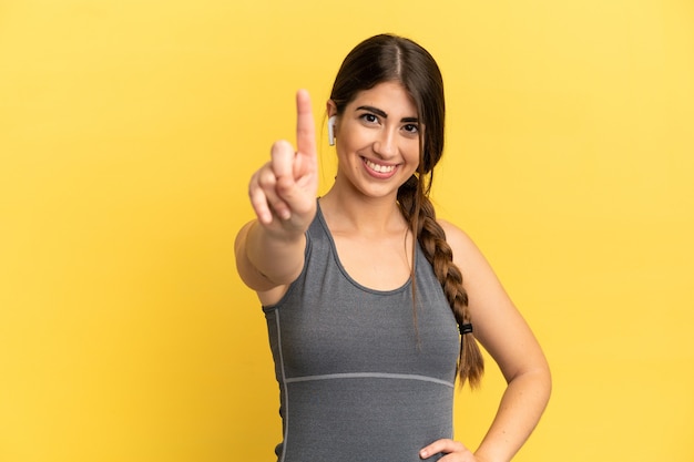 Femme caucasienne sportive isolée sur une surface jaune montrant et levant un doigt