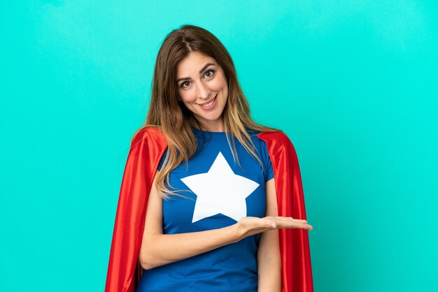 Femme caucasienne de super héros isolée sur fond bleu présentant une idée tout en regardant en souriant vers