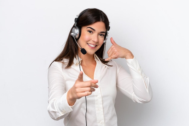 Femme caucasienne de télévendeur travaillant avec un casque isolé sur fond blanc faisant un geste de téléphone et pointant vers l'avant