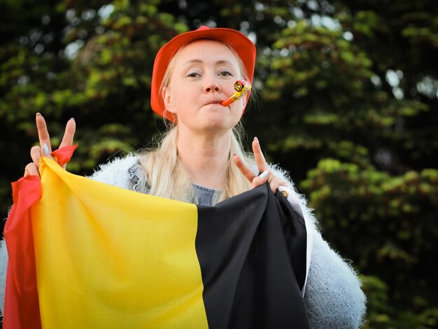 Femme caucasienne tenant un drapeau belge et soufflant un sifflet célébrant le jour de l'indépendance