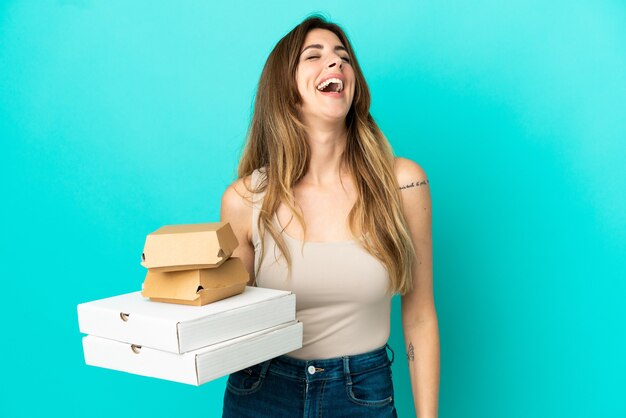 Femme caucasienne tenant des pizzas et un hamburger isolé sur un mur bleu en riant